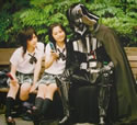 Two Japanese schoolgirls showing off their phones to Darth Vader