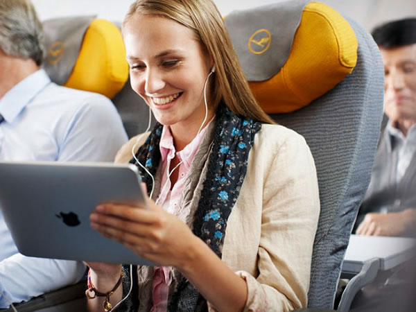 Woman sitting in airplane passenger seat, smiling as she uses an iPad