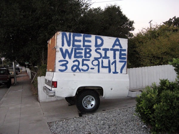 Hand-painted sign on back of truck trailer: "NEED A WEBSITE 325-9417"