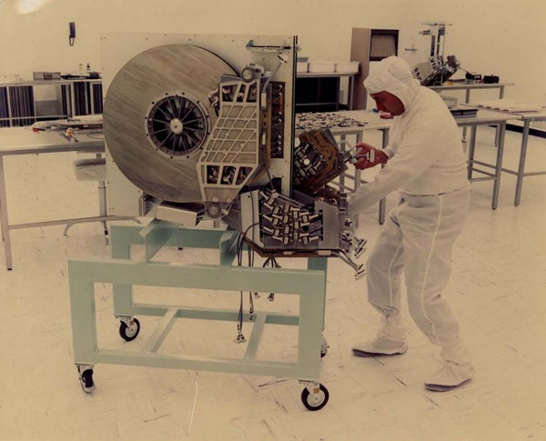 Late '60s/early '70s photo of man in "clean suit" pushing a giant hard drive on a cart in a computer room.