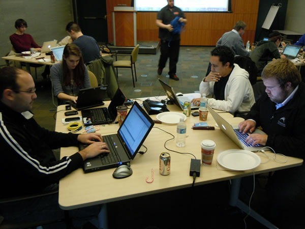 title Four developers working on their laptops, gathered around a single table