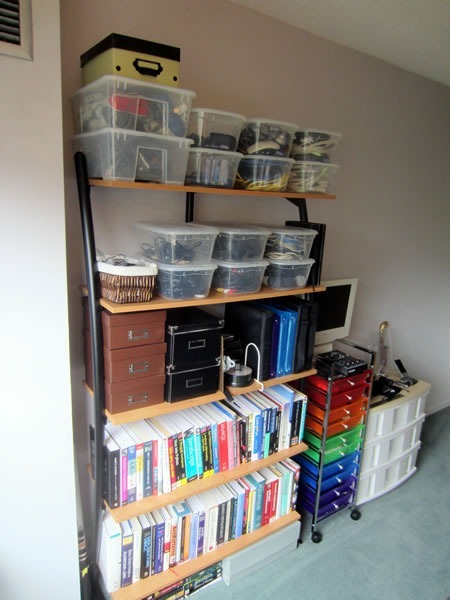 Bookshelves packed with books, plus photo boxes of files and many plastic bins full of wiring and other tech equipment