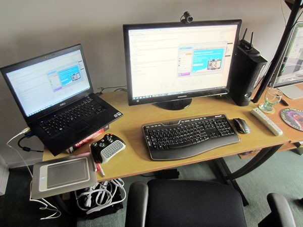 The left side of Joey's workstation, with a Dell 15" laptop, 25" Samsung monitor, Wacom drawing tablet, Xbox and wireless controller and office chair