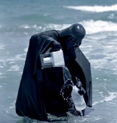 Darth Vader standing in the ocean, pouring water from a Brita pitcher into a plastic jug