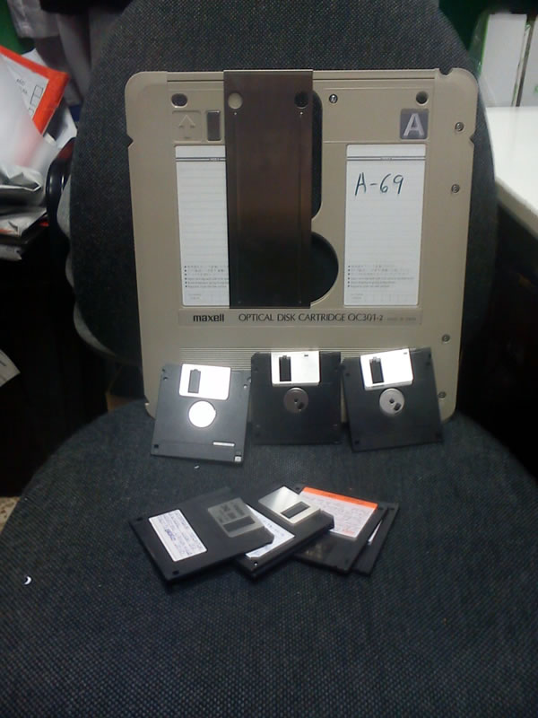 Optical disk cartridge propped up on an office chair, dwarfing the 3.5 inch floppy disks surrounding it