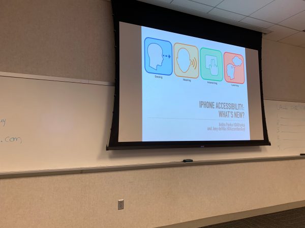 Close-up of the presentation screen, showing the presentation title slide: 'iPhone accessibility: What's New? by Anitra Pavka and Joey deVilla'. Taken January 30, 2020 at Tampa Bay UX Group meetup at the Kforce office in Tampa.