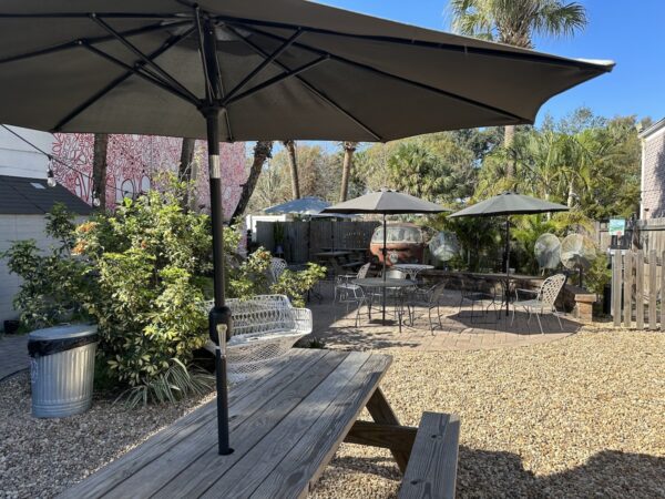 The courtyard at Spaddy’s Coffee in Seminole Heights, Tampa. It’s an open space sandwiched between two one-storey buildings with picnic and patio tables, and palm trees. The sky is blue and cloudless.