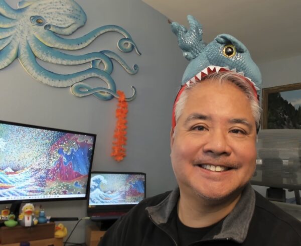 Joey de Villa smiles in his office, wearing a headband that looks like a blue dragon biting into his head.